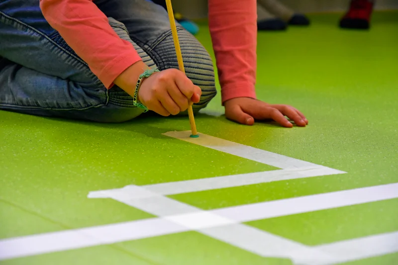 Ein Kinder fährt mit einem Stab eine Linie auf dem Boden nach